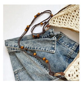 Détail du sac bandoulière en paille avec perles en bois et anneau métal sur du denim