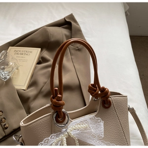Détail du cabas beige avec texture grainée, poignée nouée marron et charms dentelle et perle