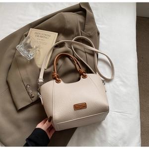 Détail du cabas en cuir beige avec poignée ronde marron et nœuds décoratifs