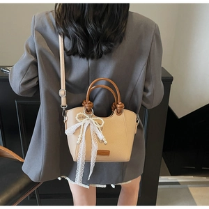 Détail du sac à main beige en cuir grainé avec nœud en dentelle et perles et anses brunes