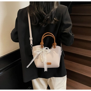 Détail du sac cabas en cuir beige avec nœud en dentelle, perle et poignées marron