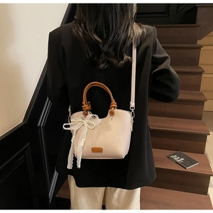 Détail d'un sac cabas en cuir beige avec nœud en dentelle et pendentifs en perles