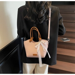 Détail du sac cabas rose clair avec nœud en dentelle blanche et poignées marron sur escalier