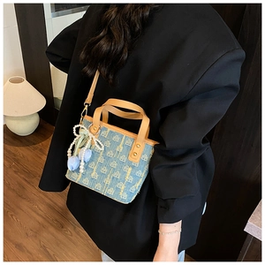 Dettaglio borsa a secchiello in denim blu con tracolla in pelle e ciondolo a fiori