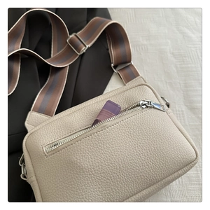 Detail of beige litchi leather crossbody bag with striped strap and silver zipper pocket