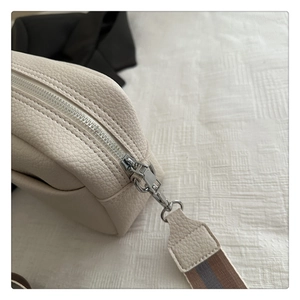 Detail of lychee textured beige crossbody bag with metal zipper and striped strap