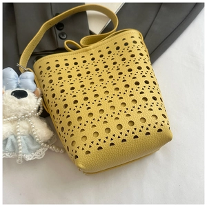 Détail du sac seau jaune en cuir ajouré orné d'un pendentif en peluche petit chien blanc