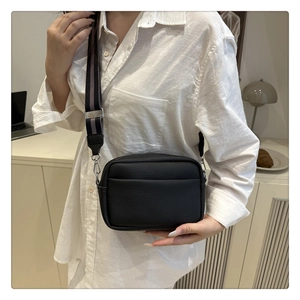 Detail of black lychee texture crossbody bag with striped woven strap on white shirt