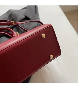 Detailansicht der roten Ledertasche mit schützenden goldenen Metallfüßen und Trageriemen