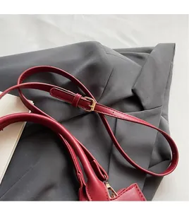 Detail einer roten Ledertasche mit verstellbarem Schultergurt und goldfarbenen Schnallen