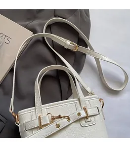 Detail of white mini handbag featuring adjustable shoulder strap and gold buckle hardware