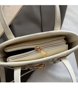 Close-up of golden zipper puller and crocodile embossed leather on cream white bag