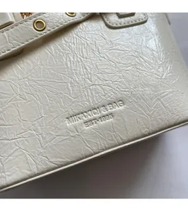Macro detail of white textured leather with embossed MIKAXIQI branding and gold metal rings
