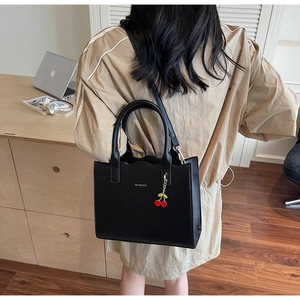 Close-up of structured black leather tote bag with cherry pendant and shoulder strap
