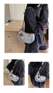 Close-up of a metallic silver half-moon bag featuring a cute doll pendant and lock detail