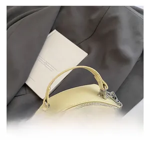 Detail der hellbeige gesteppten Rundtasche mit Tragegriff und Silberbeschlägen