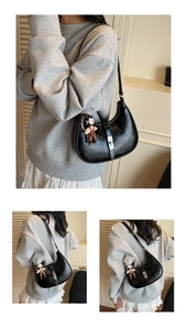 Detail of black pleated moon bag with silver buckle, cartoon charm, and pearl strap