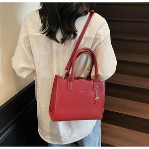 Detail of red leather tote bag with scalloped edge and cherry charm held by a model