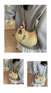 Detail of yellow crescent shoulder bag featuring silver buckle and cartoon plush pendant