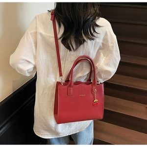Detail of red bridal tote bag with gold logo, scalloped edges, and cherry charm