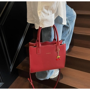 Red leather tote bag with cherry charm held by a model on wooden stairs