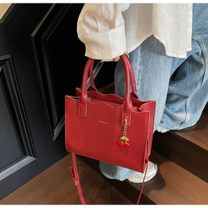 Detail of red wedding tote bag with wave-edge design and cherry charm accessory