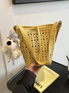 Sac seau jaune ajouré moderne avec breloque ours perlé sur une table en bois sombre