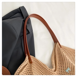 Detail of beige crochet tote bag with brown leather handles and a blue bow charm