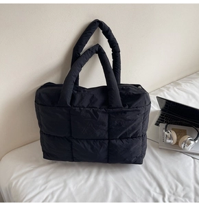 Detailed view of black quilted puffer tote bag on a bed with lifestyle work accessories