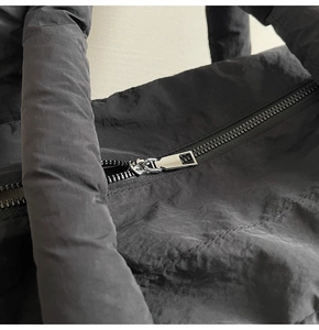 Detail of black quilted tote bag with silver metal zipper and padded shoulder handle