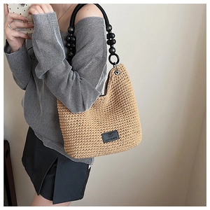 Close-up of woven bucket bag featuring black beaded strap and leather logo patch