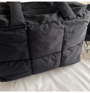 Macro detail of black quilted tote bag showing puffer fabric texture and zipper closure