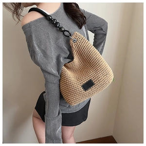 Detail of woven bucket bag featuring unique black beaded strap and leather logo patch
