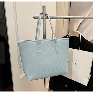 Detail of light blue quilted tote bag with gold stud accents hanging in shop display