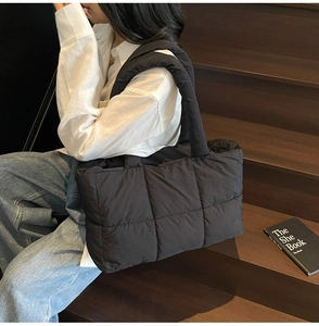 Close-up of black quilted puffer tote bag with padded strap on a seated model