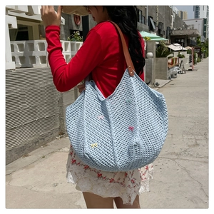 Detail of light blue woven tote bag with colorful bows and brown leather straps