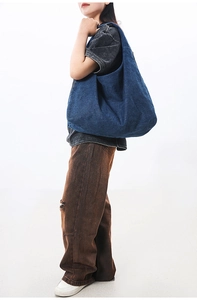 Detail of blue denim shoulder bag showing washed texture and silver zipper detail
