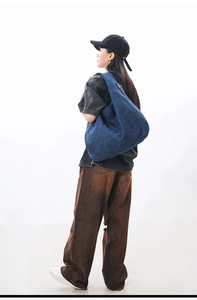 Detailed side view of a large blue denim hobo bag worn by a model in a casual style