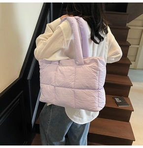 Detailed view of lavender quilted tote bag with wide shoulder strap worn on wooden stairs