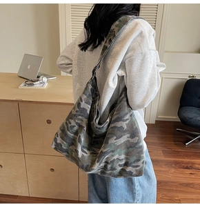 Detail of a large camouflage canvas tote bag worn by a model in a modern room