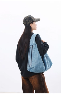 Detail of light blue denim hobo bag featuring dual vertical parallel zipper pockets