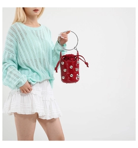 Détail d'un sac seau en cuir verni rouge avec rivets argentés et poignée en métal