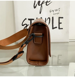 Detail view of brown leather box bag featuring wide textile strap and black metal hook