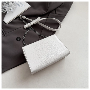 Macro shot of white crocodile embossed texture and silver chain strap on small square bag