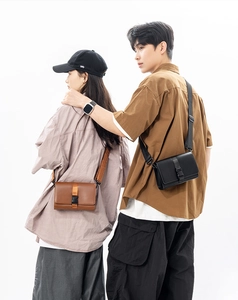 Detail of couple wearing matte leather box crossbody bags in black and brown colors