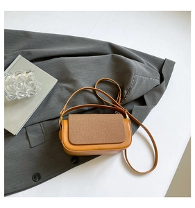 Detail of tan leather crossbody bag with woven texture flap on a grey blazer background