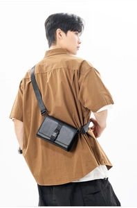 Detail of male model wearing a black matte rectangular crossbody bag with buckle closure