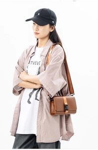 Detail view of brown leather messenger bag with wide strap and plastic buckle on male model