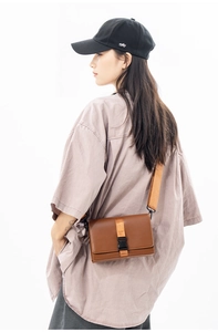 Detail showing the brown messenger box bag with orange textile strap and plastic buckle