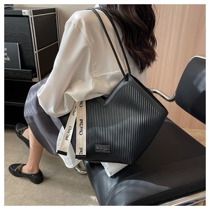 Détail d'un sac cabas noir plissé à rayures verticales avec ruban décoratif lettré chic